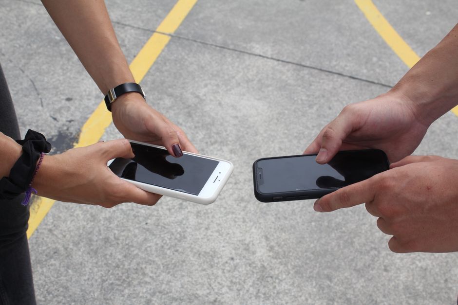 Two people holding their smartphones out toward each other on a parking lot, representing different AI assistants giving different answers