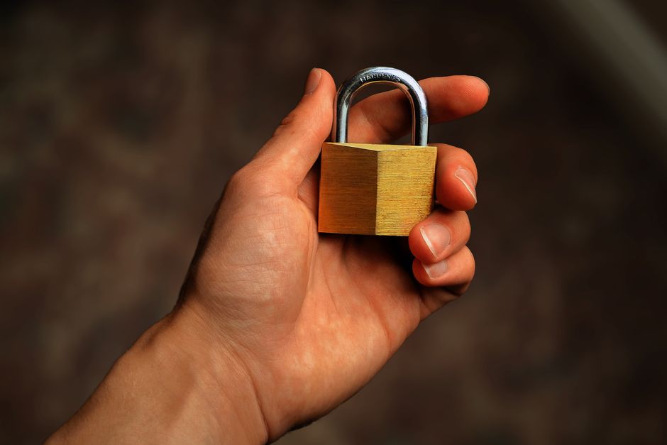 A hand holding a brass padlock against a dark background, representing keeping your Instagram data export private