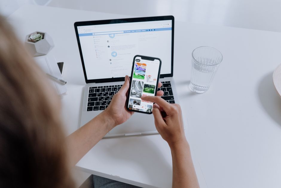A person at a desk holding a smartphone next to an open laptop, representing comparing ways to see who unfollowed you on Instagram