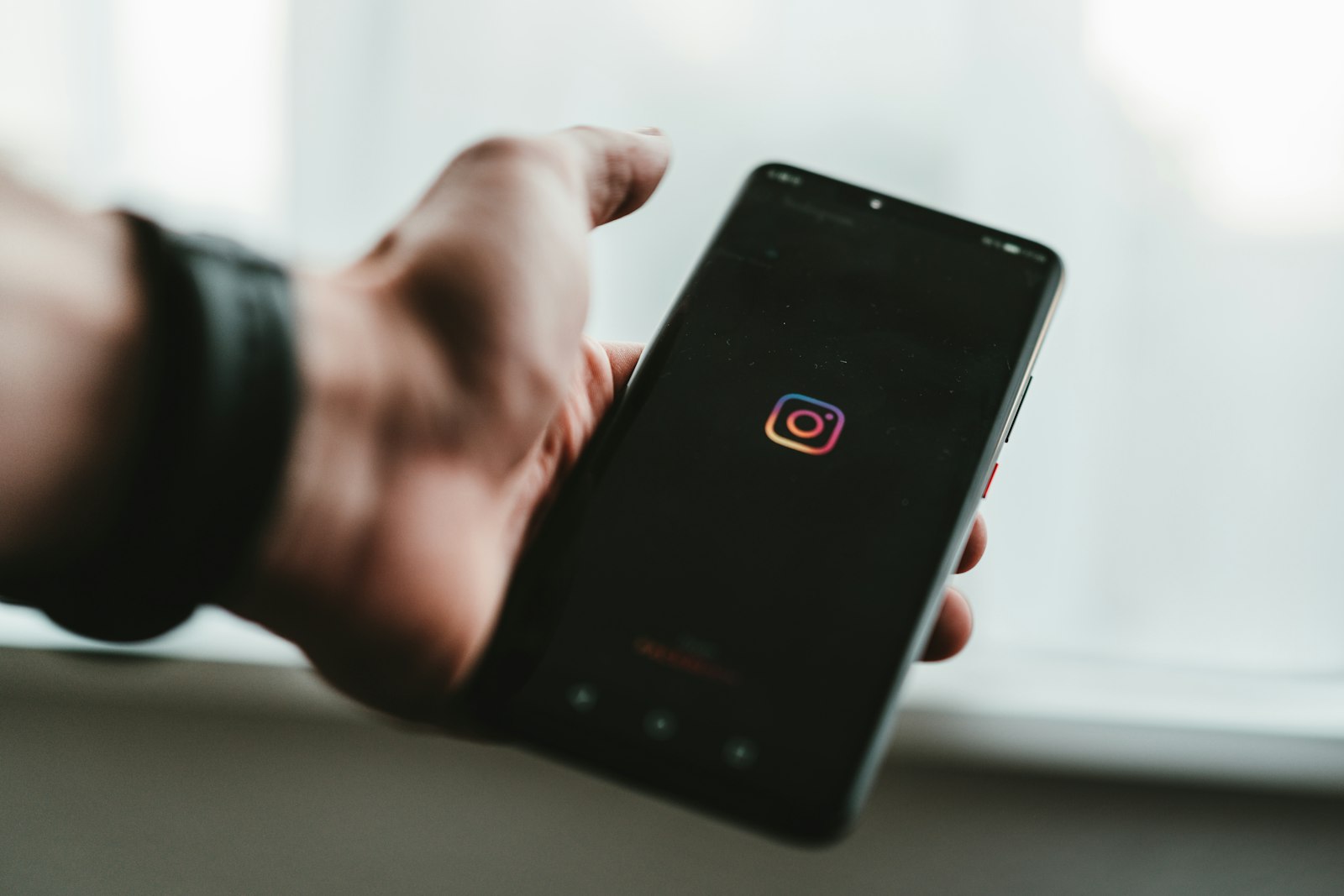 A hand holding a phone with the Instagram logo on the screen