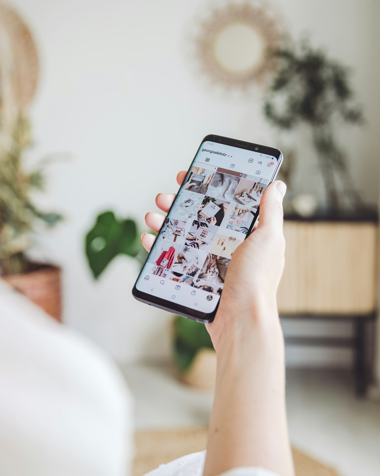 A hand holding a phone open to an Instagram profile grid