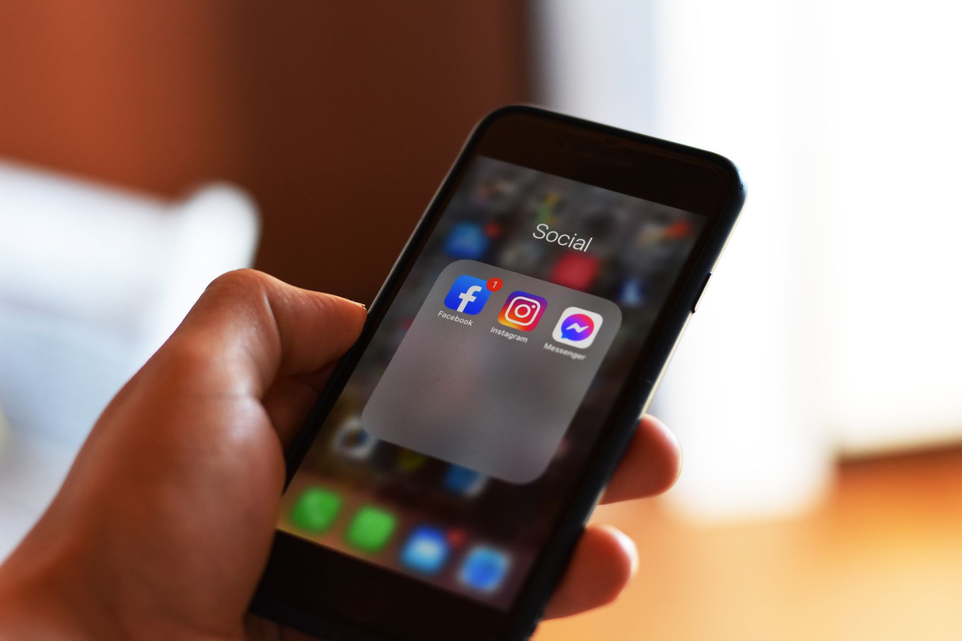 A hand holding a smartphone showing social media apps, representing checking whether someone noticed an unfollow and refollow on Instagram