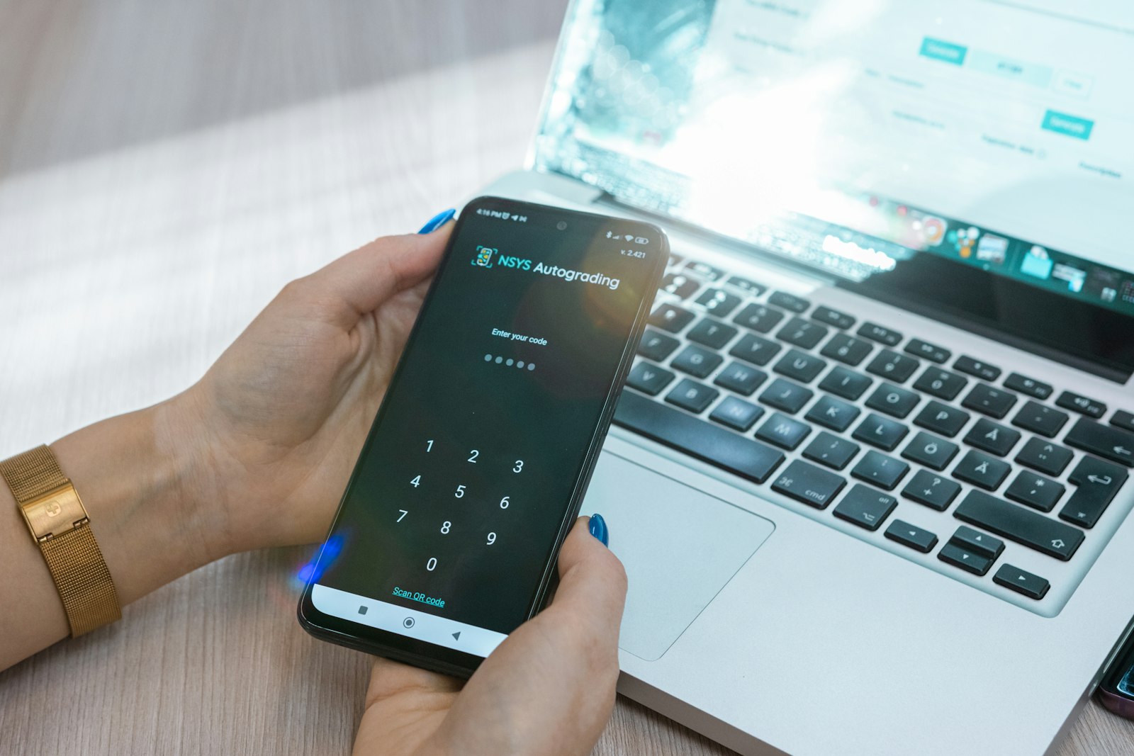 A hand holding a phone beside a laptop, entering a numeric code to unlock an account